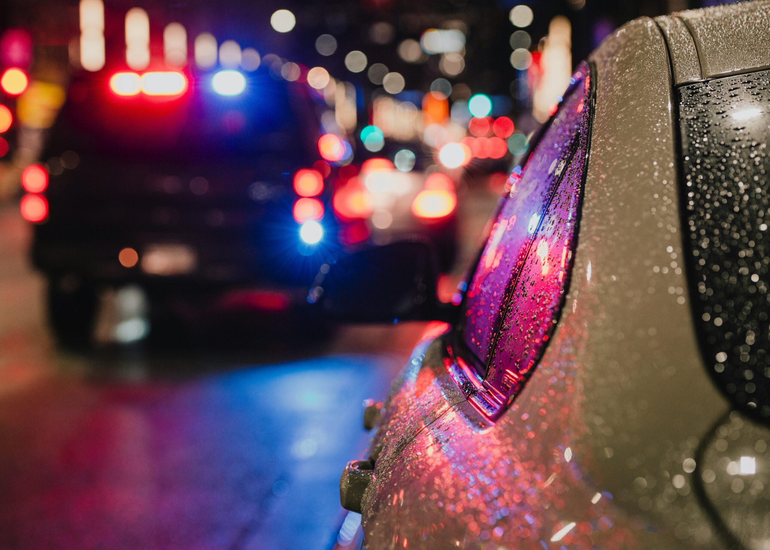 albert-stoynov-PiEBY75vv5Q-unsplash Police car in rain at night with lights on.